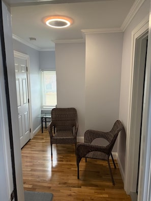 A hallway with wooden flooring, two wicker chairs, a glass table, and a ceiling light fixture. - Charming 3-bedroom apartment in lovely Utica (Utica)