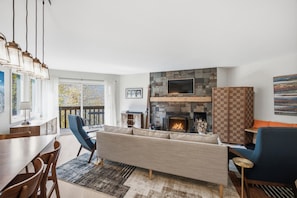 A modern living room with a fireplace, a sofa, a dining area, and a view of the outdoors. - Family friendly 3br Condo on Okemo Shuttle Route just minutes from Okemo (Ludlow)