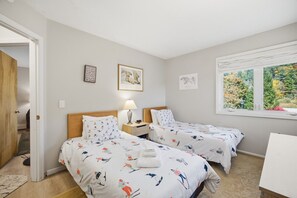 A bedroom with two beds, a nightstand, a lamp, and a window with a view of trees. - Family friendly 3br Condo on Okemo Shuttle Route just minutes from Okemo (Ludlow)