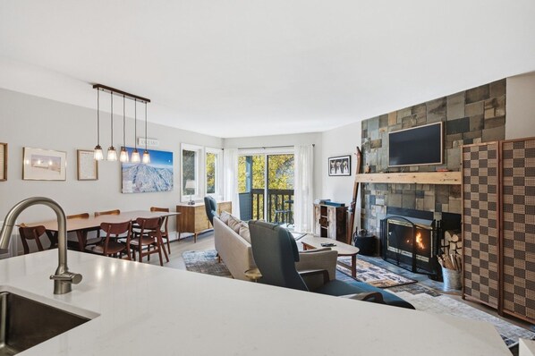A modern living room with a fireplace, dining area, and kitchen. - Family friendly 3br Condo on Okemo Shuttle Route just minutes from Okemo (Ludlow)