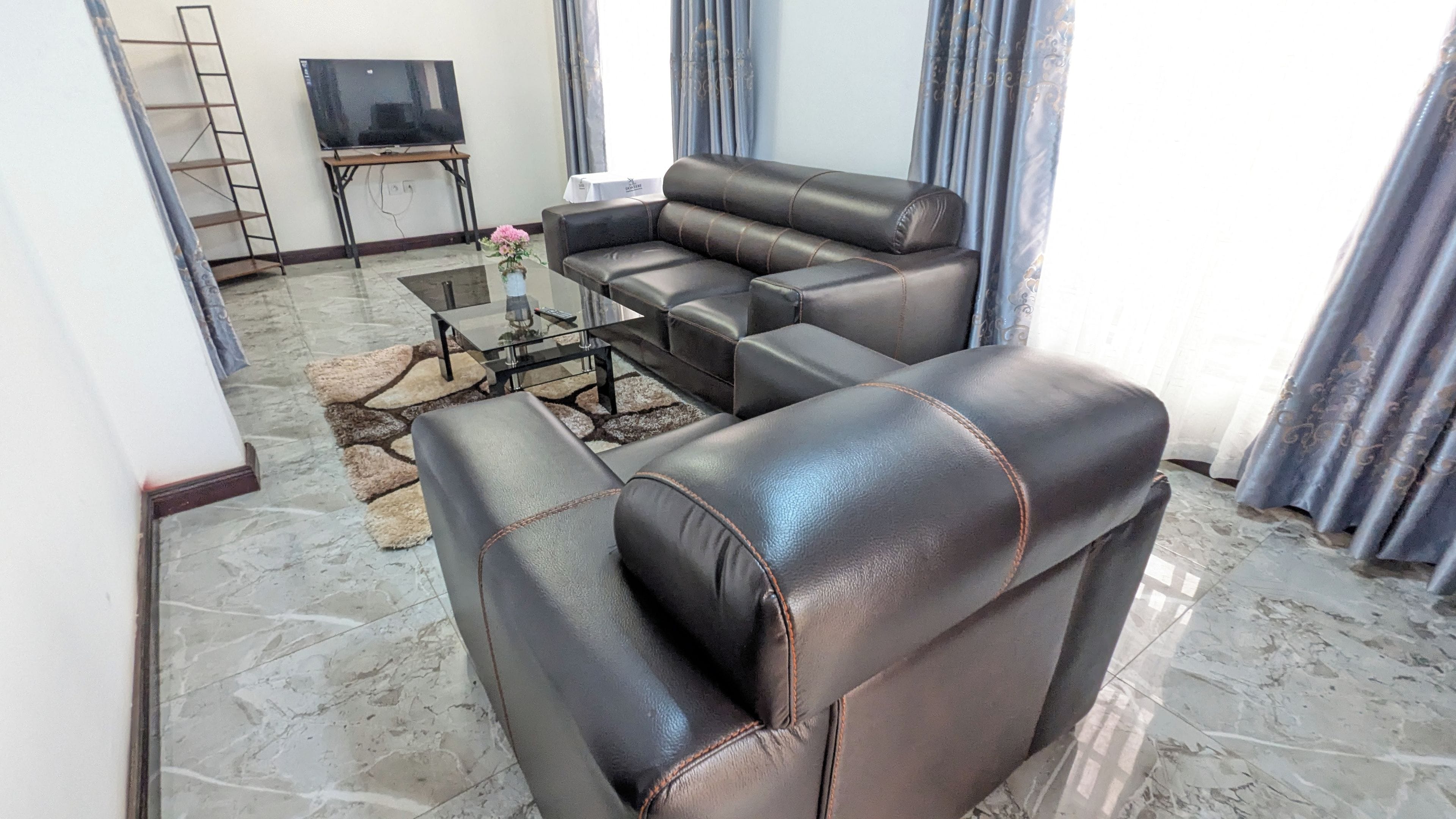 A living room with a sectional sofa, a flat-screen TV on a stand, a coffee table, and a patterned rug.