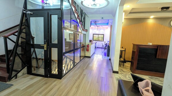 A hotel lobby with a glass elevator, a reception desk, and a fire extinguisher.