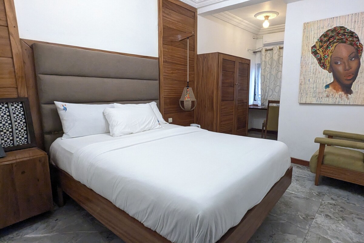 Een slaapkamer met een groot bed, een houten hoofdbord, een nachtkastje met een lamp en een stoel.
