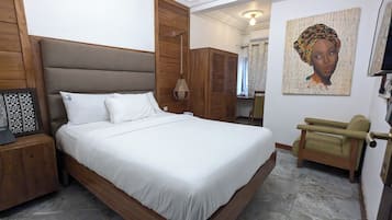 Un dormitorio con una cama grande, cabecera de madera, una mesita de noche con lámpara y una silla.