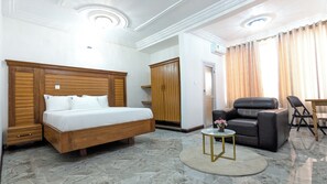 Een hotelkamer met een bed, een zithoek met een stoel en tafel, een kledingkast en een bijzettafeltje met een vaas.