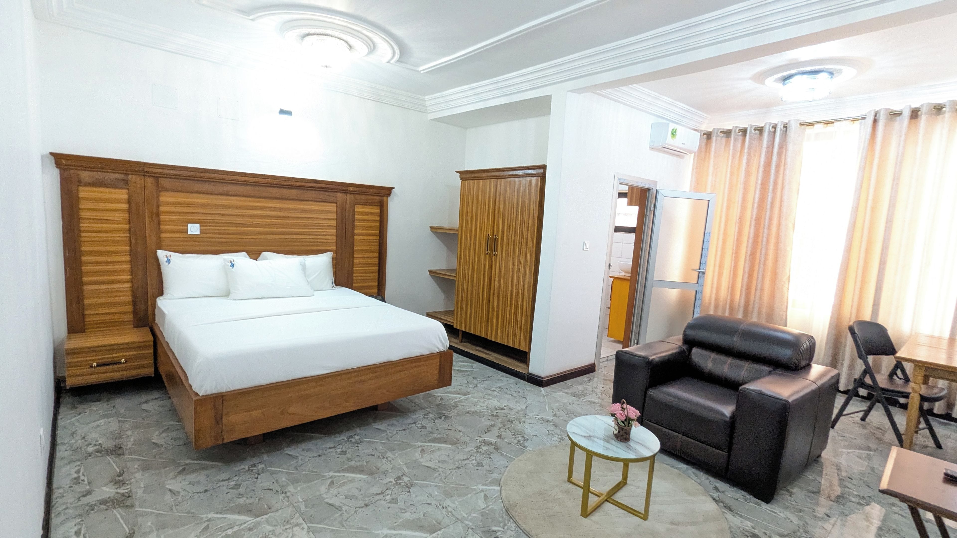 A hotel room with a bed, wardrobe, seating area, and a small table with flowers.