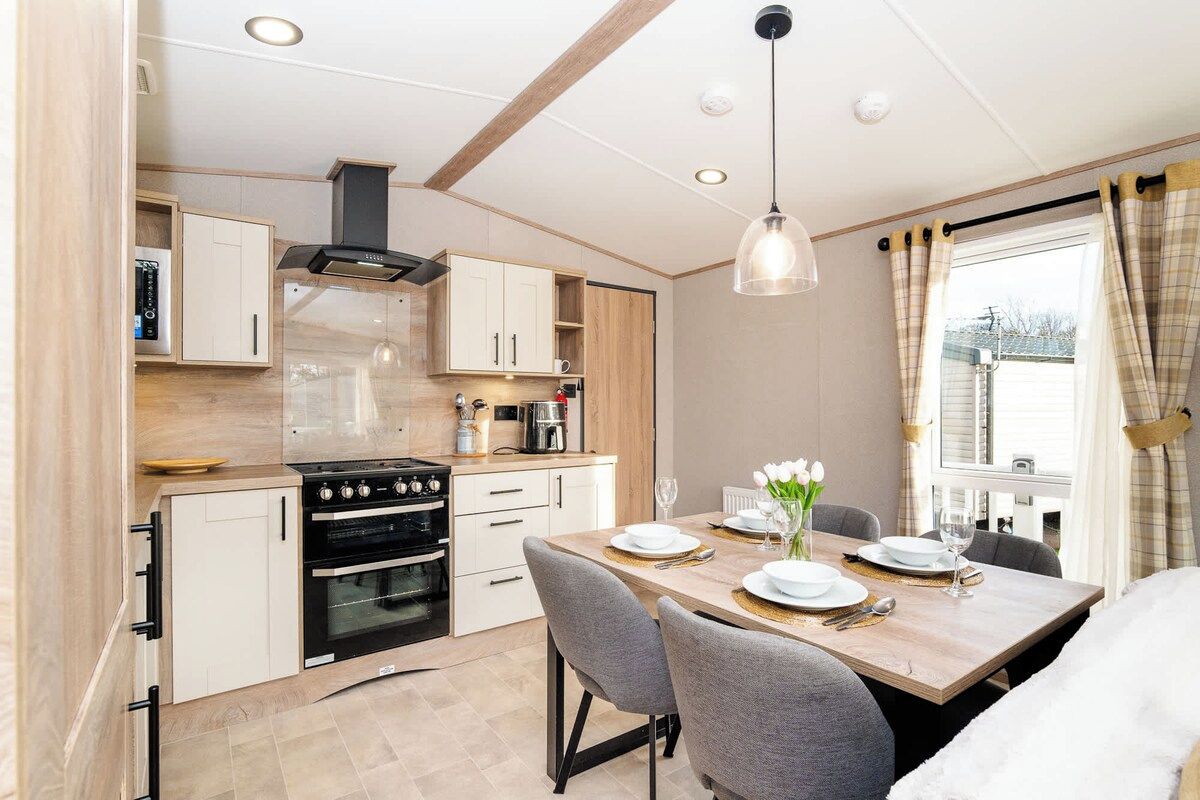 A modern kitchen with built-in appliances, a dining area with a table set for two, and a window with curtains.