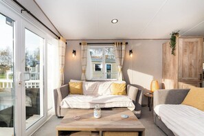 Ein gemütliches Zimmer mit einer Couch, einem kleinen Tisch und einem Schrank. Ein Fenster mit Vorhängen bietet einen Blick nach draußen.