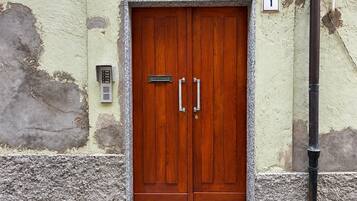 Una puerta doble de madera con un picaporte metálico y una placa, ubicada en una pared con textura y un cartel con un número.