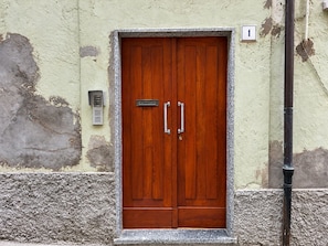 A wooden double door with a metal handle and a nameplate, set in a textured wall with a number sign above it.