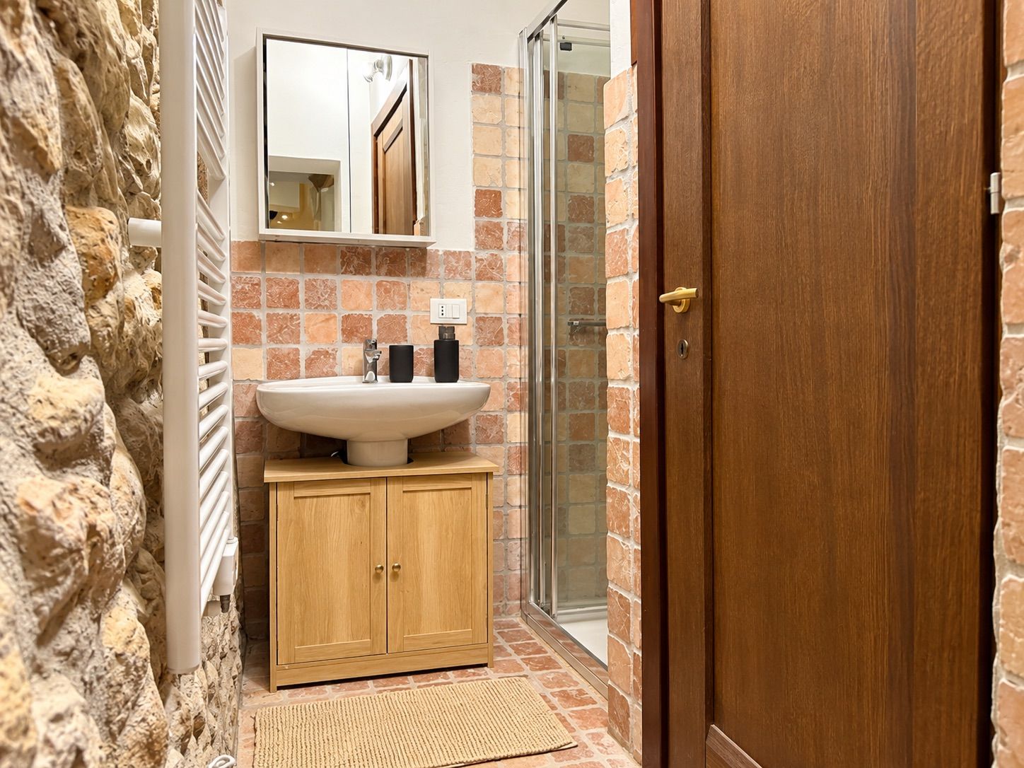 Ein Badezimmer mit Steinwand, Waschbecken mit Spiegel, Dusche und Holzschränken.