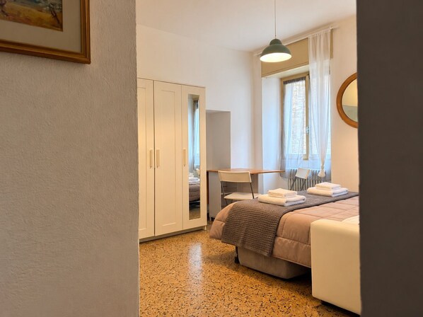 A bedroom with a bed, a desk, a chair, a wardrobe, and a window with curtains.