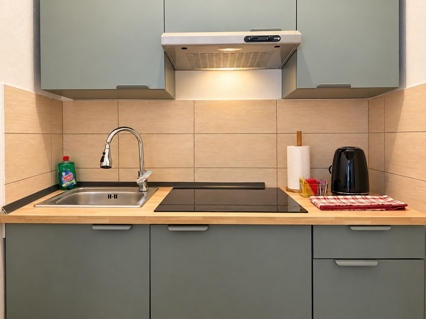 Una cocina con un lavamanos de acero inoxidable, una tetera y una botella de jabón para lavar platos.