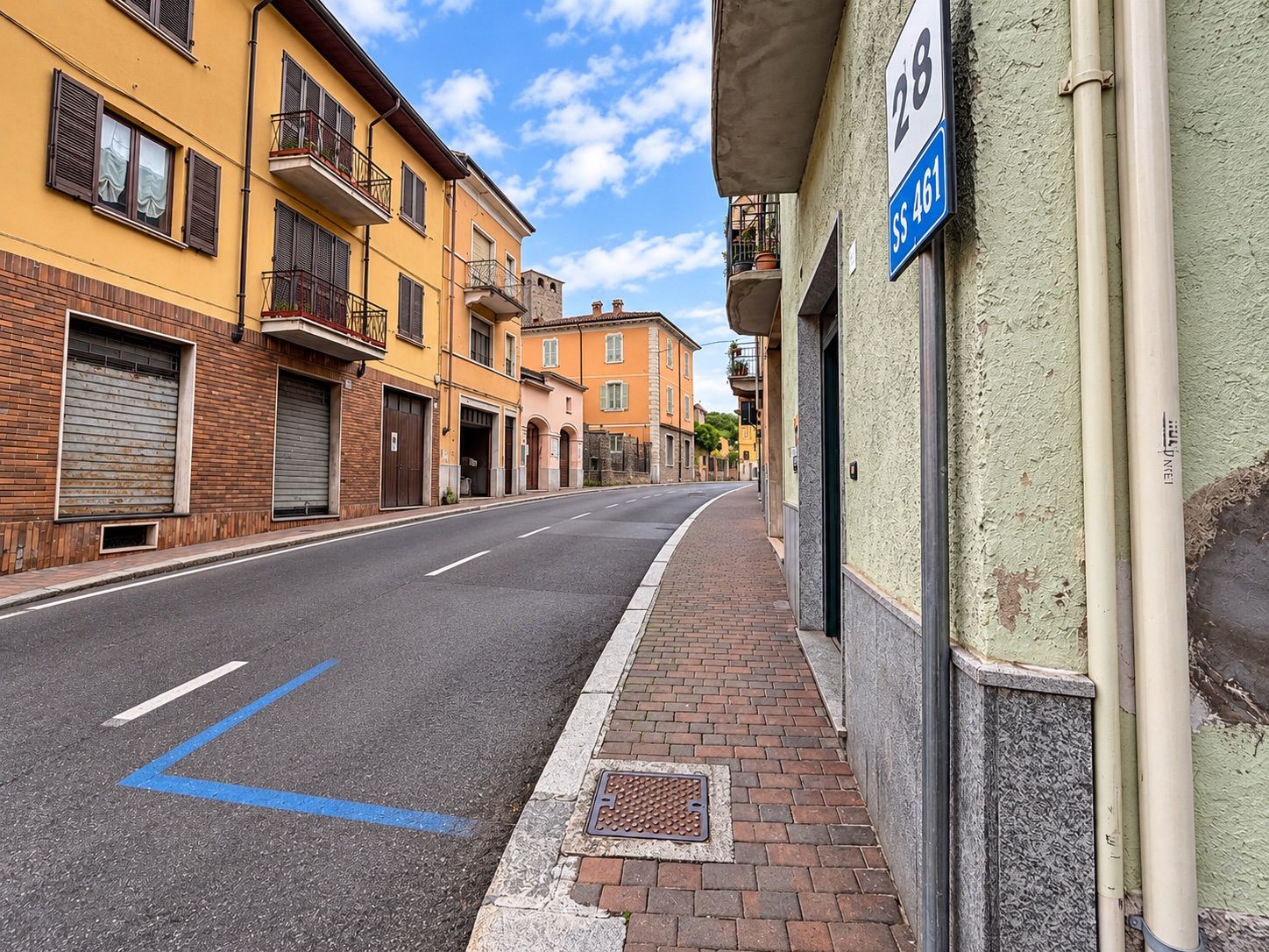 A street with buildings, a sidewalk, and a blue line marking on the road.