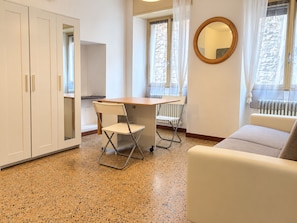 A room with a kitchenette, a dining table with chairs, a sofa, and a round mirror on the wall.