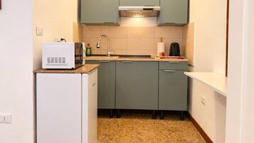 A compact kitchen with a microwave on a small fridge, a sink with a faucet, and a stove.