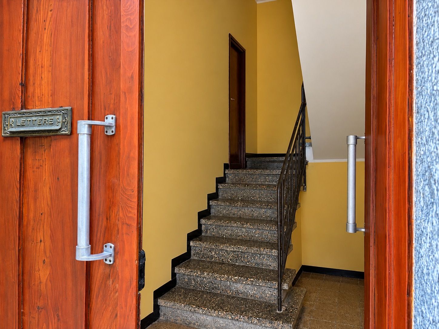 A wooden door with a metal handle and a sign, a staircase with a metal railing, and a yellow wall.