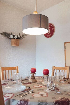A dining table set with plates, glasses, and cutlery, a hanging light fixture, and a wall-mounted sign. - Alpine Apartment with Parking - on slopes (Méribel)