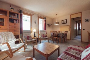 A cozy living room with a wooden coffee table, a sofa, a dining table with chairs, and a bookshelf. - Alpine Apartment with Parking - on slopes (Méribel)