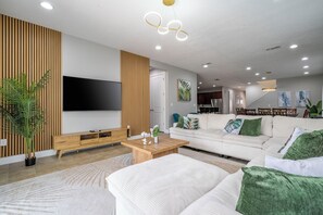 A modern living room with a flat-screen TV, wooden panel wall, white sofa, and a coffee table. - The best 11-bedroom house with a game room and spa (Kissimmee)