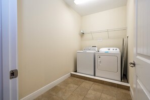 A laundry room with two washers and dryers, a metal shelf above, and a door to the right. - The best 11-bedroom house with a game room and spa (Kissimmee)