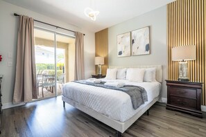 Ein Hotelzimmer mit einem großen Bett, einem Nachttisch, einer Lampe und Blick ins Freie.