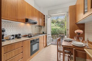 A kitchen with wooden cabinets, a built-in oven, a sink, and a dining area with a table and chairs. - Apartment 'Aurora Alta' with Balcony, Wi-Fi and Air Conditioning (Maslianico)