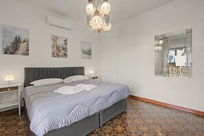 Un llit ben fet amb un panell frontal gris, una làmpada de nit i un aire condicionat fixat a la paret.