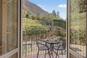 Un balcó amb taula i cadires, amb vista a un paisatge muntanyós amb una tanca i vegetació.