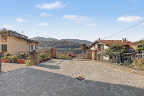 Un carrer pavimentat que condueix a una zona residencial amb cases, un paisatge de muntanya al fons i un cel serè.