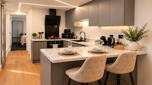 Een moderne keuken met een centraal eiland, barkrukken en uitzicht op de aangrenzende slaapkamer.