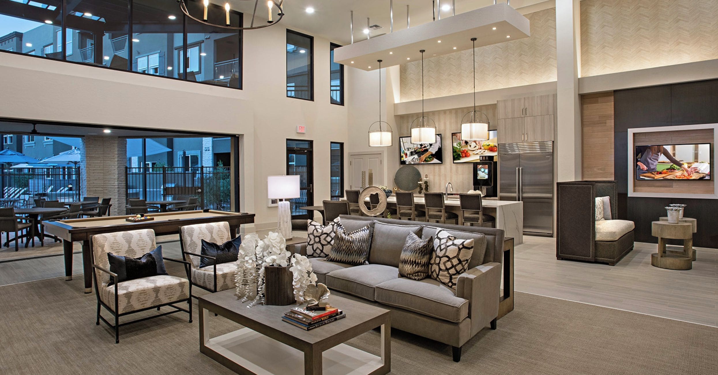 A spacious living area with a large sofa, coffee table, and dining area. There is a kitchen with a refrigerator and a TV mounted on the wall.