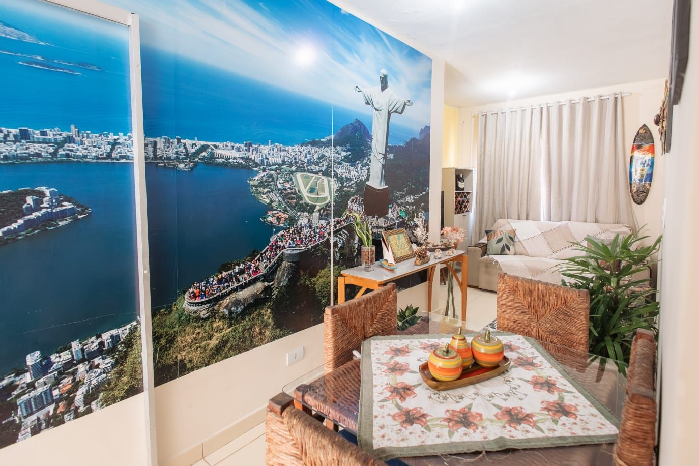 Une pièce décorée d’une grande fresque représentant un paysage urbain, avec un canapé, une table ornée d’objets décoratifs et une plante en pot.