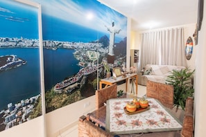A room with a large cityscape mural, a sofa, a table with decorative items, and a potted plant. - Comfortable and peaceful, that's what we call our cozy retreat. (Itacaré)