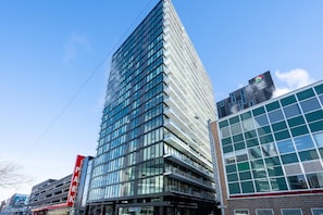 Een modern hoog gebouw met een glazen gevel, een opvallend rood bord dat een parkeerplaats aangeeft, en een zichtbaar logo aan de zijkant.