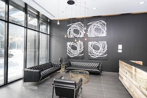 Un vestíbul modern amb un sofà de pell negra, una taula de cafè de vidre i obra d'art abstracta a la paret.
