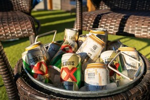 Un vassoio di metallo colmo di lattine di birra assortite, tra cui marchi come Dos Equis e HUSS Brewing Co., posizionato all'aperto su un prato.