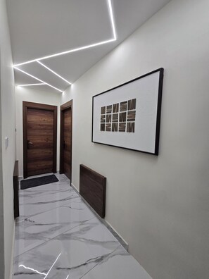 A hallway with a marble floor, a framed artwork on the wall, and wooden doors. - Luxury 3BD with Open View Roof (Amman)