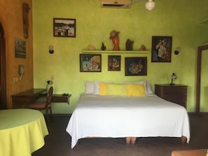 A room with a bed, a desk, and a chair. There are paintings on the wall and a shelf with decorative items. - Awesome studio with AC in the best location in Barra de Navidad (Barra de Navidad)