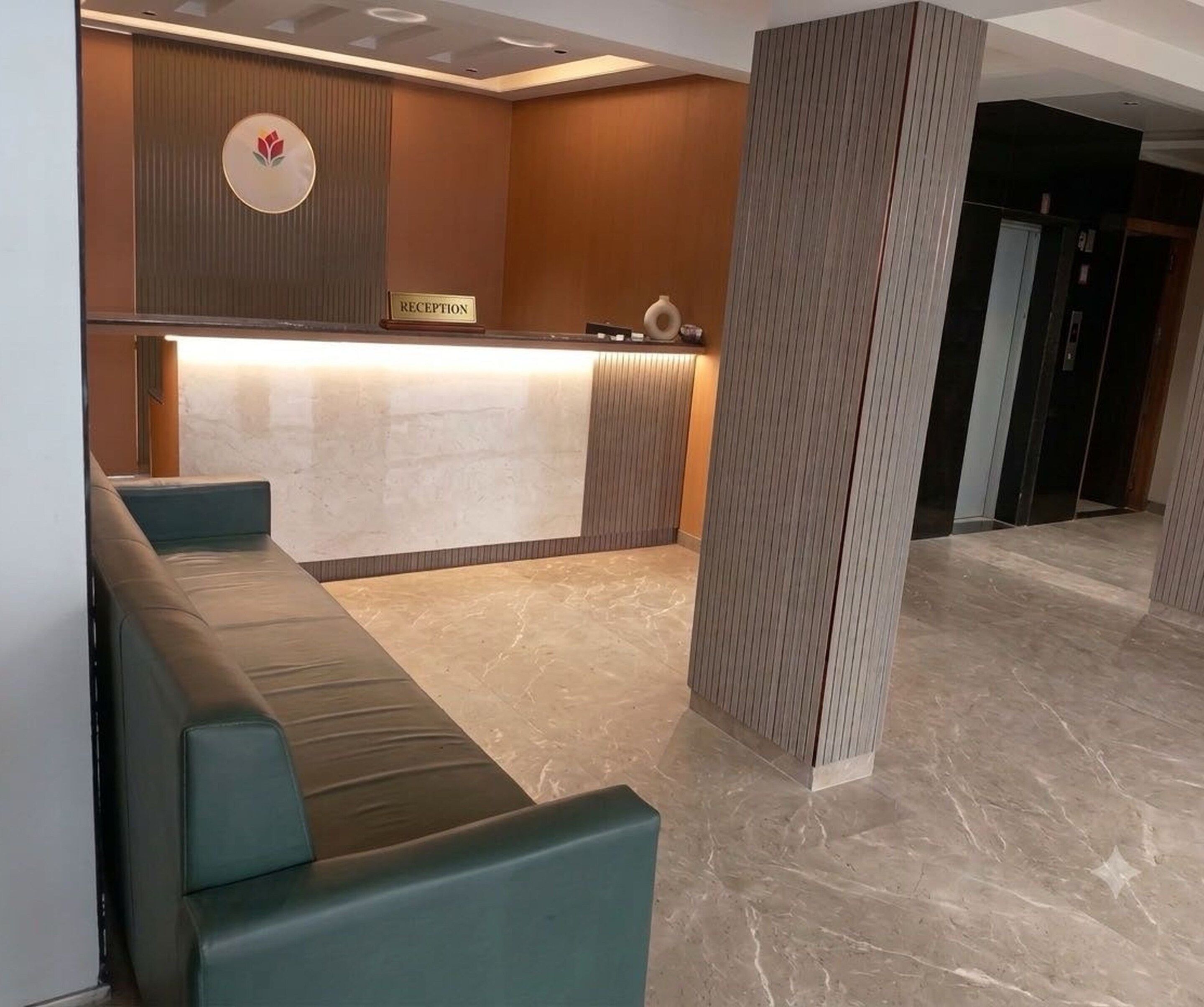 Un espace d’accueil comprenant un comptoir de réception, un coin salon avec des bancs rembourrés et un pilier orné d’un motif texturé.