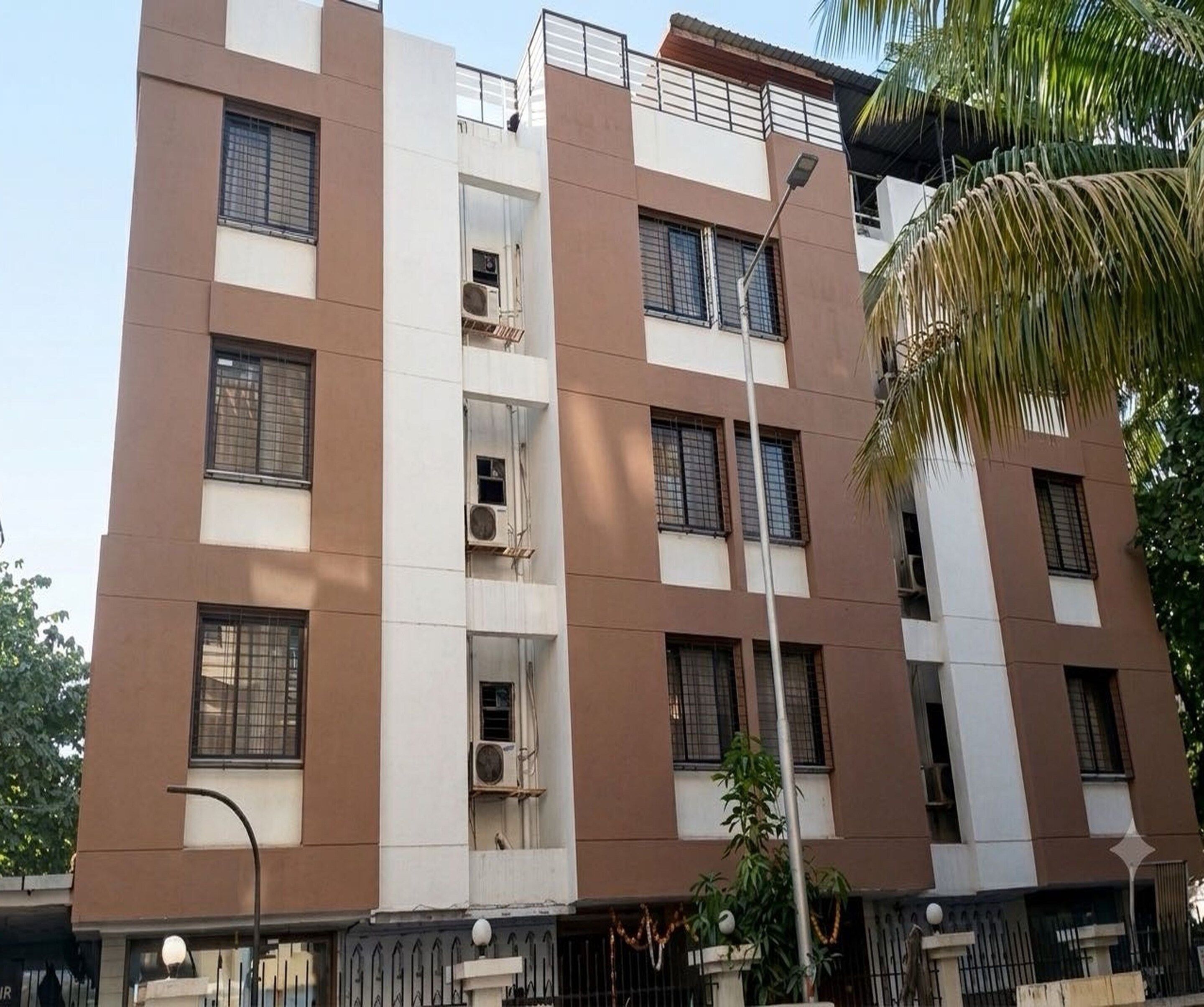 Un immeuble résidentiel à plusieurs étages, doté de balcons, de climatiseurs et d’une entrée sécurisée par un portail.