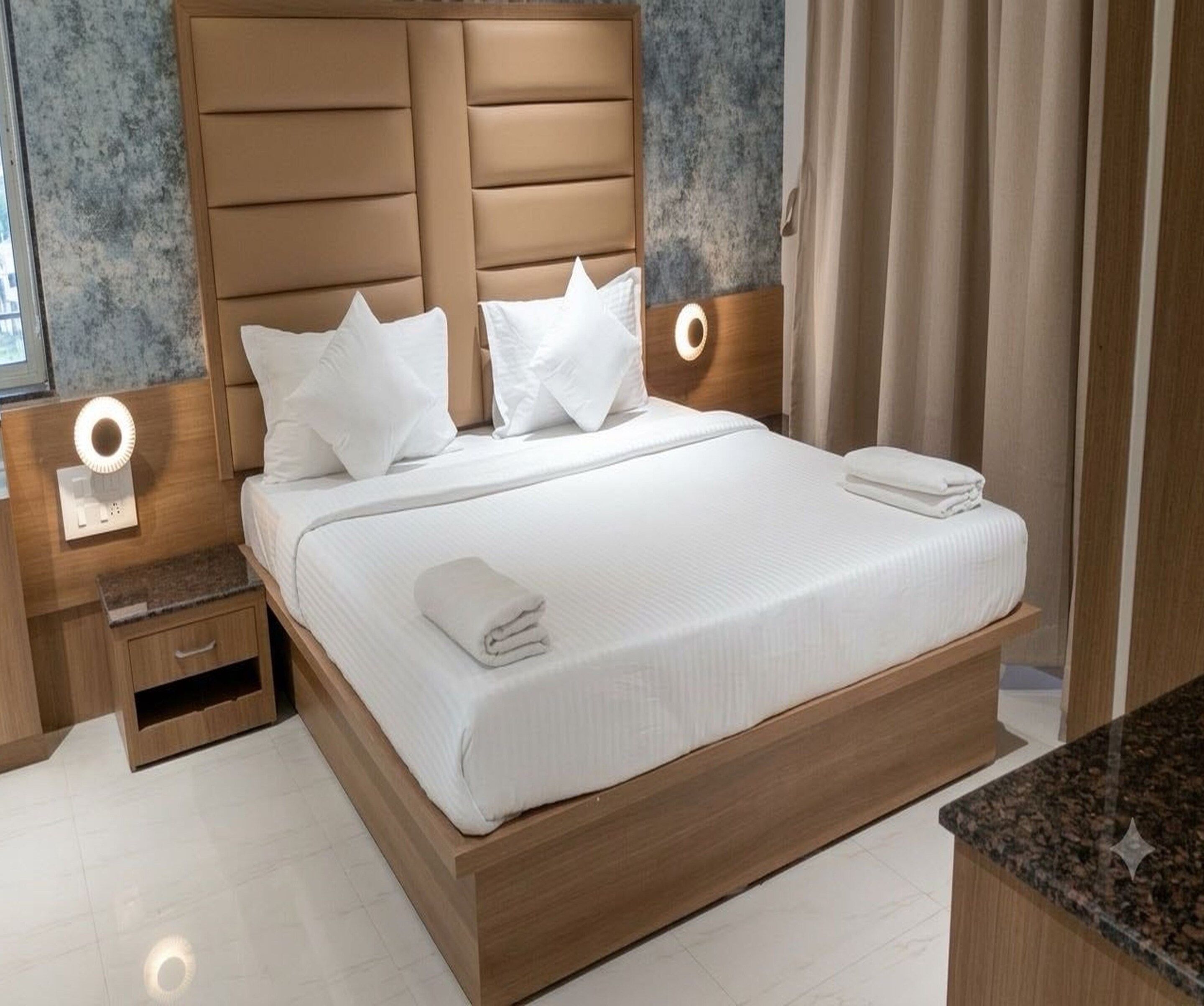Cama bem arrumada com lençóis e almofadas brancos, cabeceira de madeira e abajures laterais.