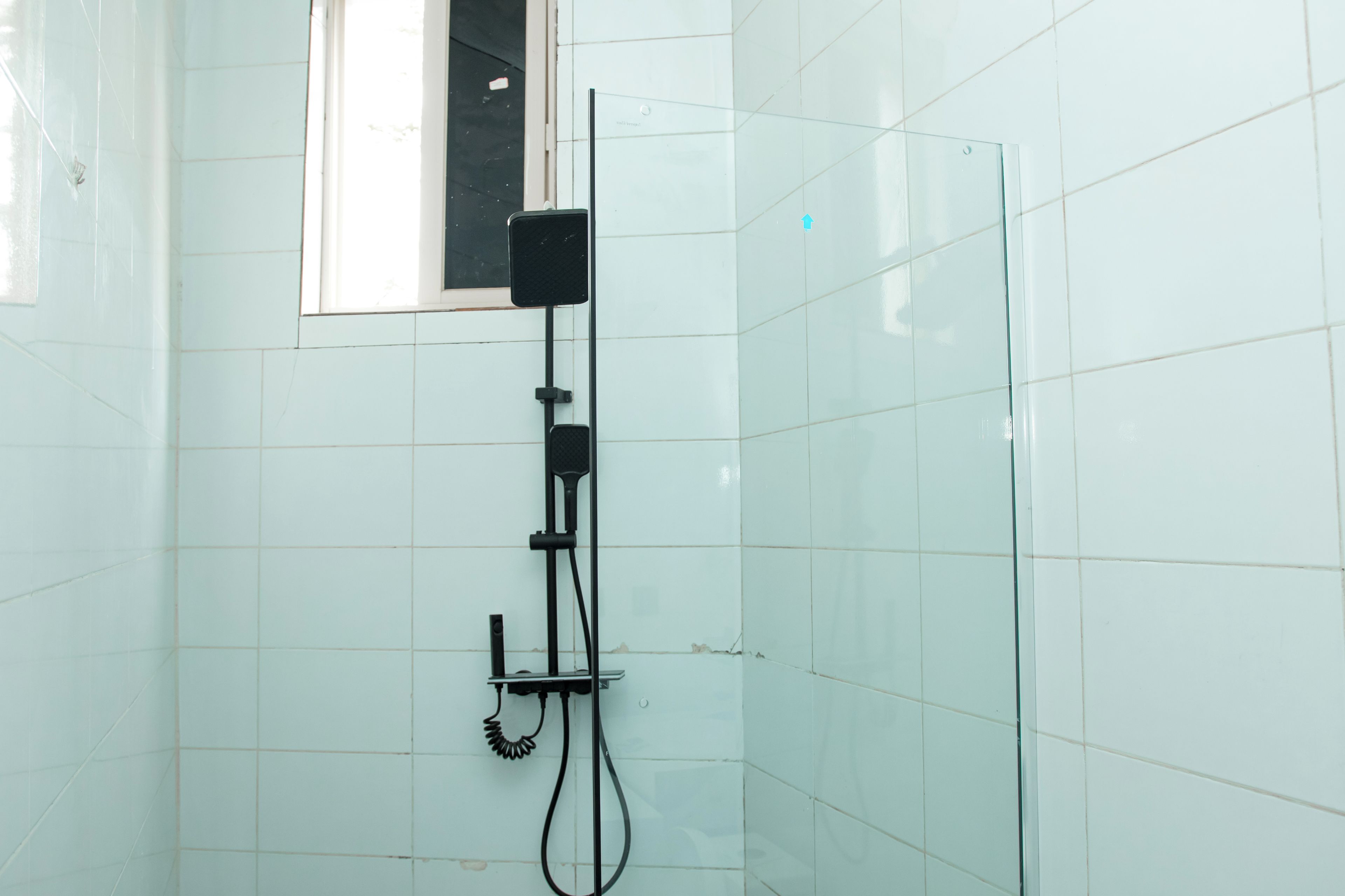 A shower area with a handheld showerhead, a control panel, and a glass partition.