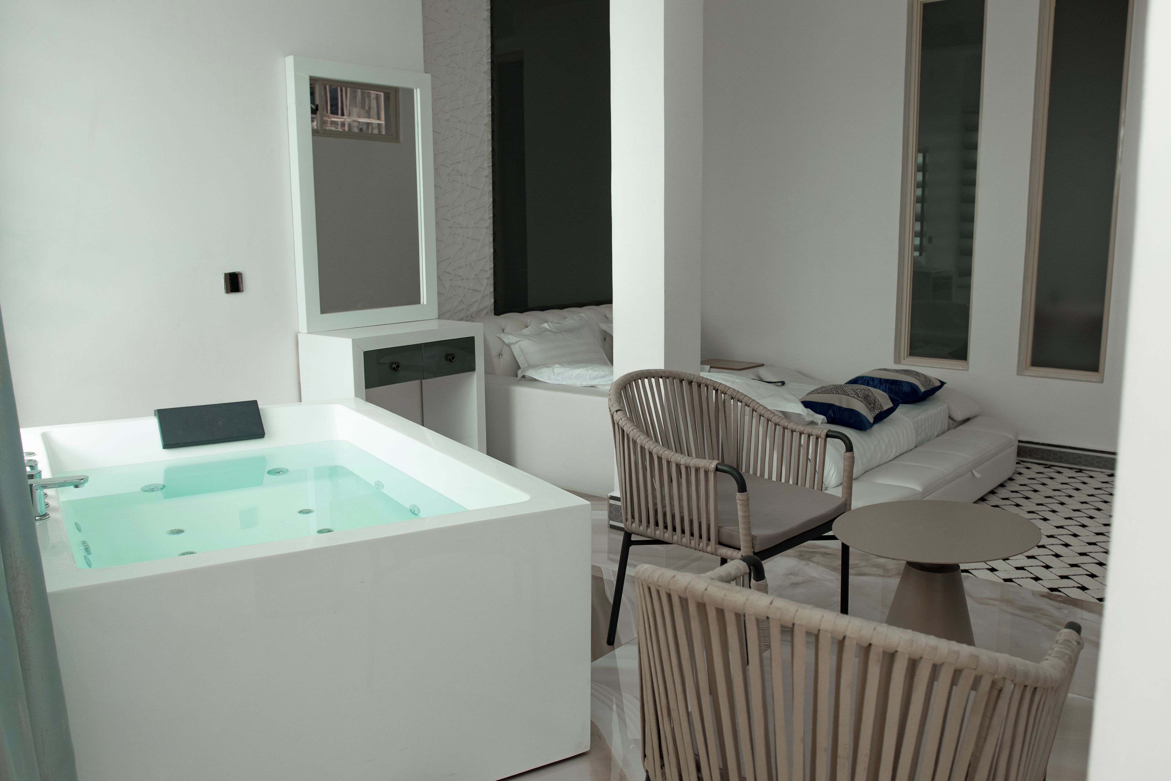A modern bathroom with a large bathtub, a mirror, a sofa, and a chair.
