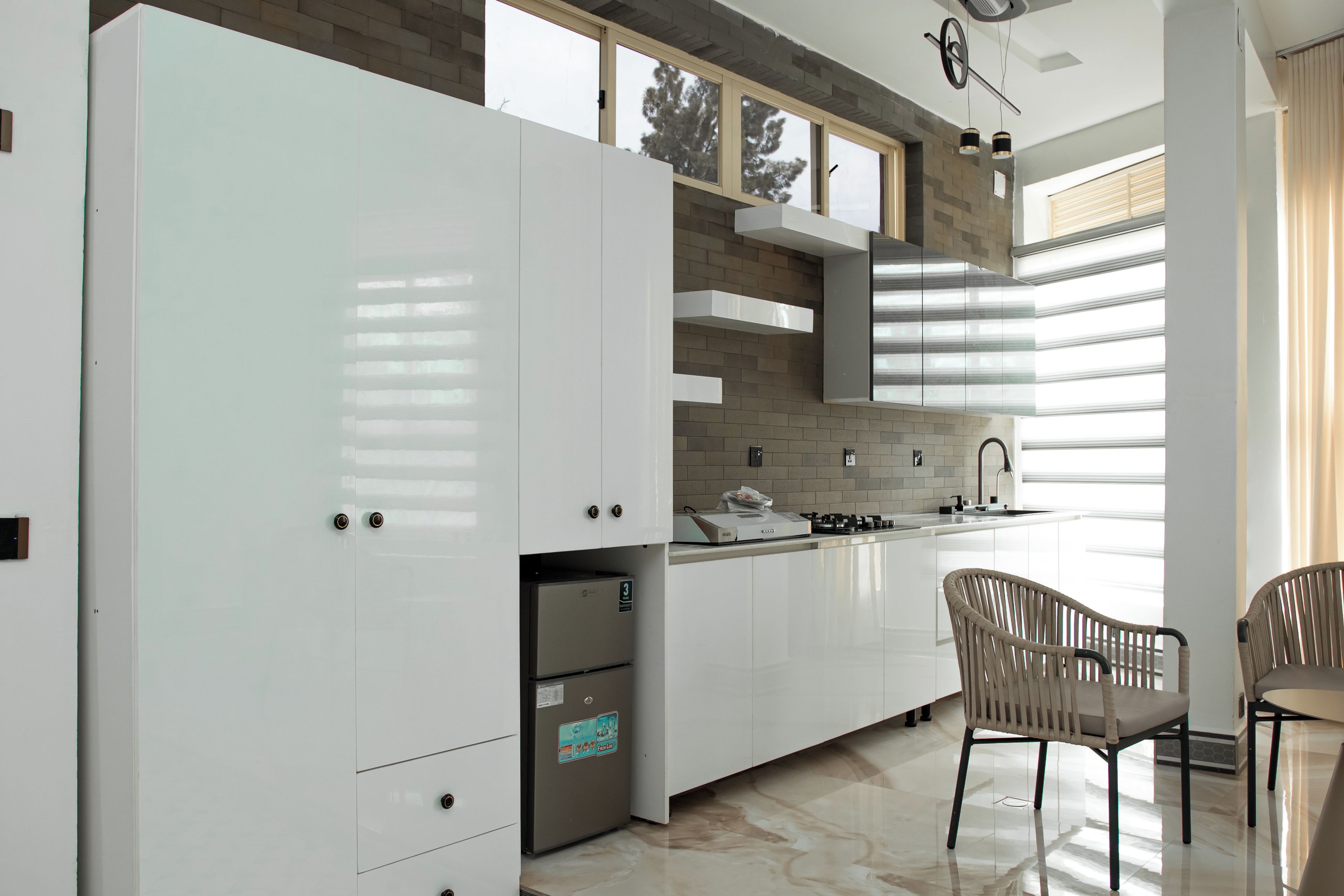 Una cocina moderna con muebles blancos, estufa integrada y un comedor con dos sillas.