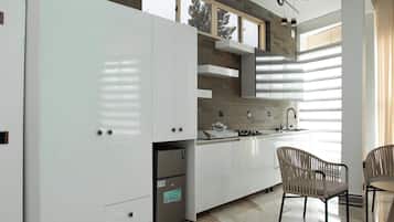 Una cocina moderna con muebles blancos, estufa integrada y un comedor con dos sillas.