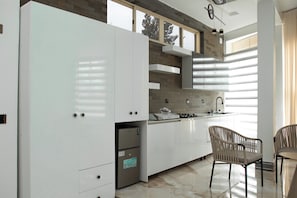 A modern kitchen with white cabinetry, a built-in stove, and a dining area with two chairs. - Neverland Boutique & Suites (Gisenyi)