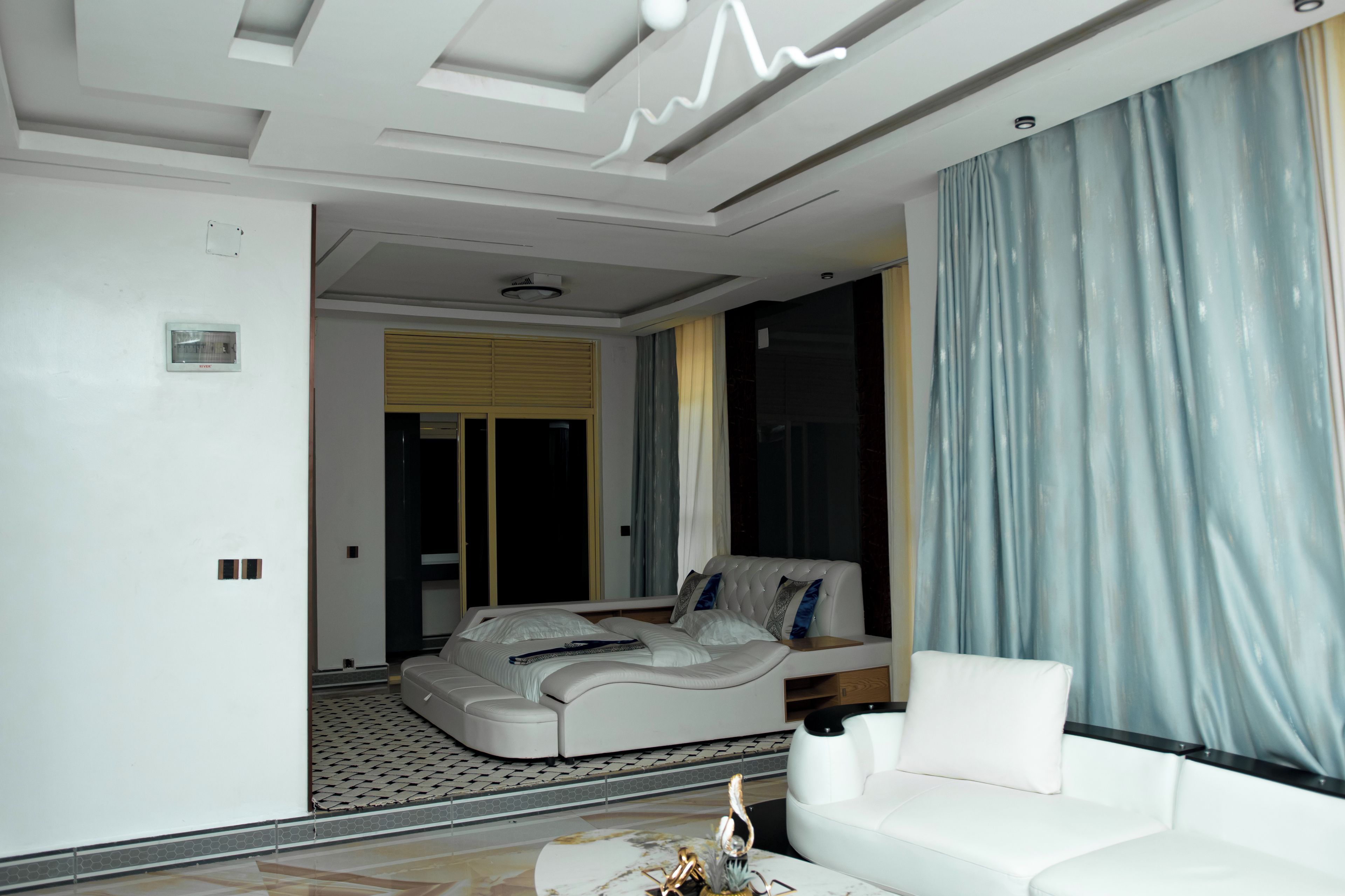 A modern living room with a sofa, a coffee table, and a large window with curtains.