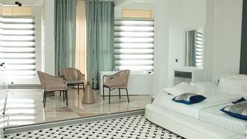 Ein modernes Hotelzimmer mit einem großen Bett, einer Sitzecke mit zwei Stühlen, einem kleinen Tisch und einem großen Fenster mit Vorhängen.
