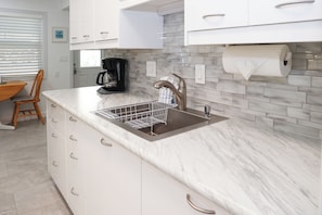 A kitchen with a marble countertop, a stainless steel sink, and white cabinets.